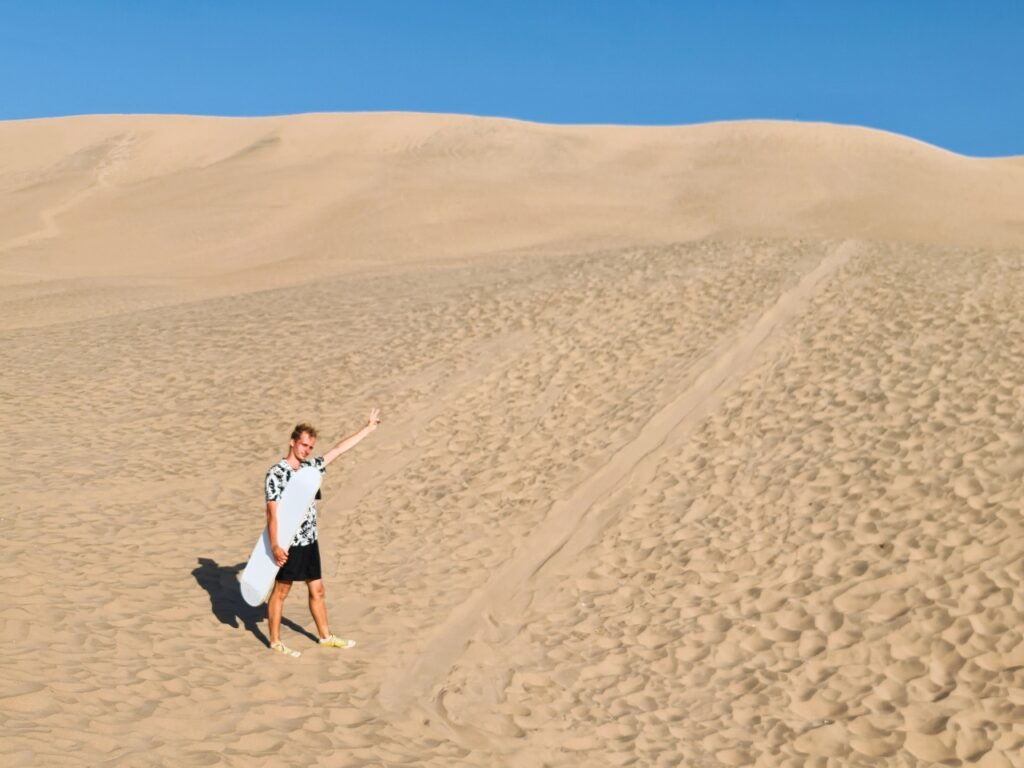 Chłopak z deską do sandboardingu na pustyni Huacachina