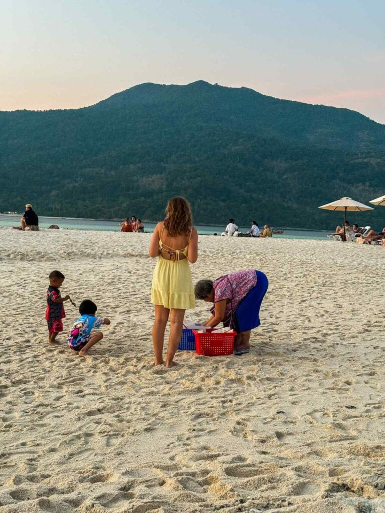 Młoda dziewczyna kupująca przekąski od lokalnej sprzedawczyni na plaży na wyspie Koh Lipe.