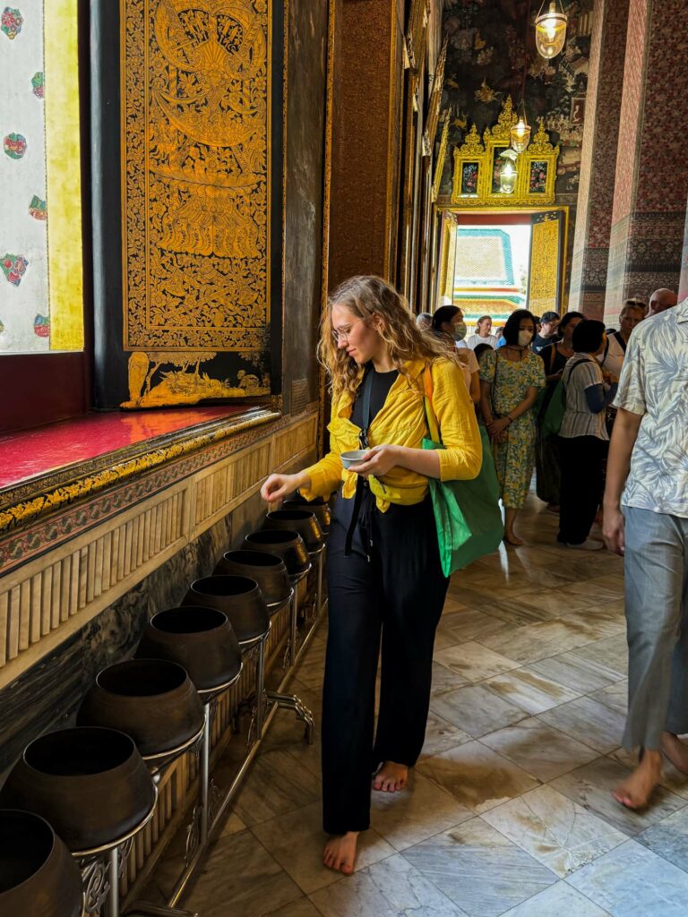 Dziewczyna wrzuca pieniądze do mis w Wat Pho w Bangkoku.