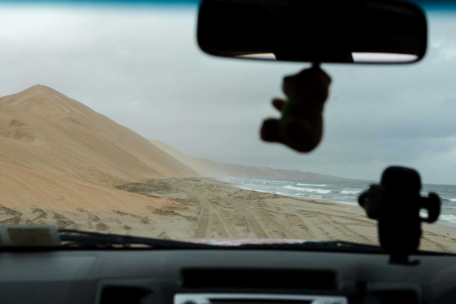 Widok z deski rozdzielczej auta jadącego plażą w Sandwich Harbour.